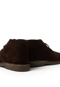 Botas de tobillo de ante marrón con una textura suave, puntera redonda y un minimalismo en los cordones. Las suelas están hechas de un goma marrón texturizada.