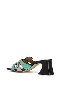 Muli con una base in pelle nera, cinturini in suede verde e grigio, e un tacco nero spesso. Dettaglio in metallo dorato notevole al centro.