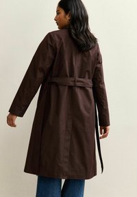 Cappotto trench marrone con cintura, maniche lunghe e taglio dritto. Tessuto liscio, design minimalistico, visto da dietro.
