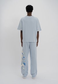 Camiseta de algodón de color azul claro con un corte relajado y mangas cortas, combinada con pantalones de chándal a juego que tienen un estampado gráfico en blanco y azul.