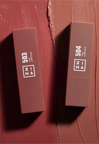 To rektangulære leppestifter i matt brun emballasje, merket 503 og 504, mot en teksturert varmtone bakgrunn med penselstrøk mønstre.