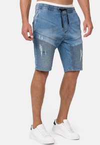 Shorts en denim de couleur bleu clair avec une coupe décontractée, une taille élastique avec cordon de serrage, des accents déchirés et un motif côtelé texturé sur les panneaux.
