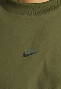 Olivgrön t-shirt med rund halsringning och ribbad krage. Har en svart Nike-logotyp tryckt på vänster bröstområde. Mjuk tygkänsla.