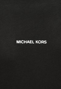 Λευκό κείμενο "MICHAEL KORS" στο κέντρο μαύρου υφάσματος, πιθανότατα είδος ρούχου.