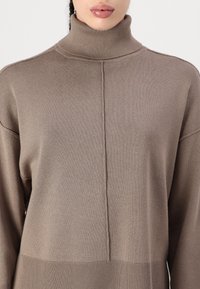 Hellbraunes Turtleneck-Pullover mit weitem Ausschnitt und gerippter Textur, ausgestattet mit einer zentralen Naht an der Vorderseite und gerippten Bündchen am Saum.