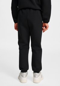 Zwarte trainingsbroek met een elastische tailleband, geribde boorden en een gladde textuur, gecombineerd met zilveren sportschoenen.