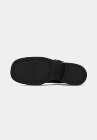 Black shoe sole featuring a textured rubber surface with horizontal and vertical ridges, and a distinctive logo imprint.