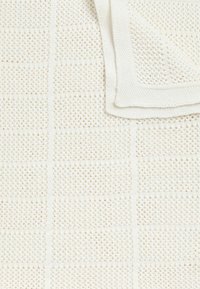 Tkaná bílá deka s mřížkovým vzorem, který má texturované detaily a hladký kontrastní lem. Měkká, lehká tkanina.