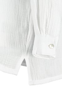 White textured shirt with a wrinkled pattern, buttoned cuff, and side slits for ease. Made from lightweight fabric.
