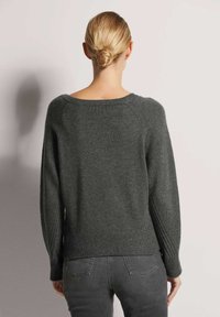 Dunkelgrauer Strickpullover mit weit geschnittenem Ausschnitt und langen, gerippten Ärmeln. Der Rücken ist etwas länger und hat eine entspannte Passform.