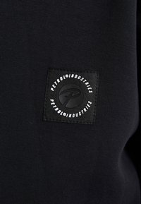 Un tejido de sudadera negro que presenta un parche rectangular de tela negra con texto circular blanco y un logo en el centro.