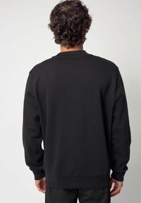 Felpa nera con maniche lunghe e polsini a coste. Tessuto morbido e texturizzato. Design a taglio dritto, con colletto a girocollo e senza loghi visibili.