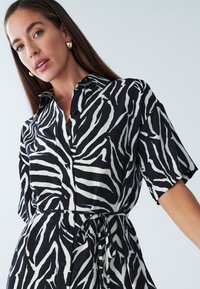 Schwarz-weißes Hemdblusenkleid mit Zebramuster, Kragen, kurzen Ärmeln und einem Bindegürtel. Verfügt über eine Knopfleiste vorne und ein strukturiertes Gewebe.