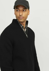 Schwarzer, gerippter Strickpullover mit einem Viertelreißverschluss-Kragen. Über einem grauen Karohemd getragen, mit einer enganliegenden Silhouette und strukturiertem Stoff.