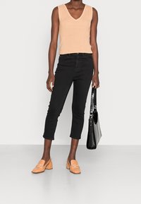 Top sin mangas de canalé beige, vaqueros recortados negros, zapatos de tacón bloque naranja y un bolso negro con grabado de cocodrilo.