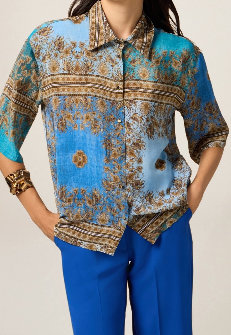 Jasnoniebieska koszula na guziki z misternymi brązowymi kwiatowymi wzorami, krótkimi rękawami i klasycznym kołnierzykiem, w połączeniu z niebieskimi spodniami.