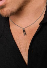 Collana in argento con un elegante pendente nero, che presenta due barre allungate attaccate nella parte superiore, che poggiano sulla pelle.