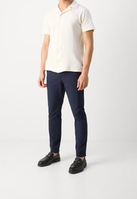 Korte mouwen crèmekleurig overhemd met gestructureerde strepen, gecombineerd met marineblauwe slim-fit broek en zwarte loafers met gouden hardware accenten.