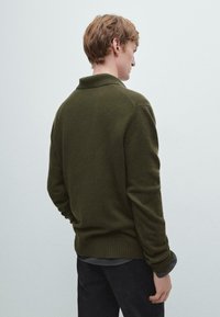 Ciemnozielony sweter z dzianiny z kołnierzykiem, prążkowanymi mankietami i dołem. Widok z tyłu pokazuje gładką teksturę i prosty design.