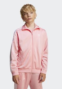 Rosa polyester treningsjakke med glidelås, ribbede mansjetter og hvite skulderstriper; har frontlommer og en liten logo på brystet.