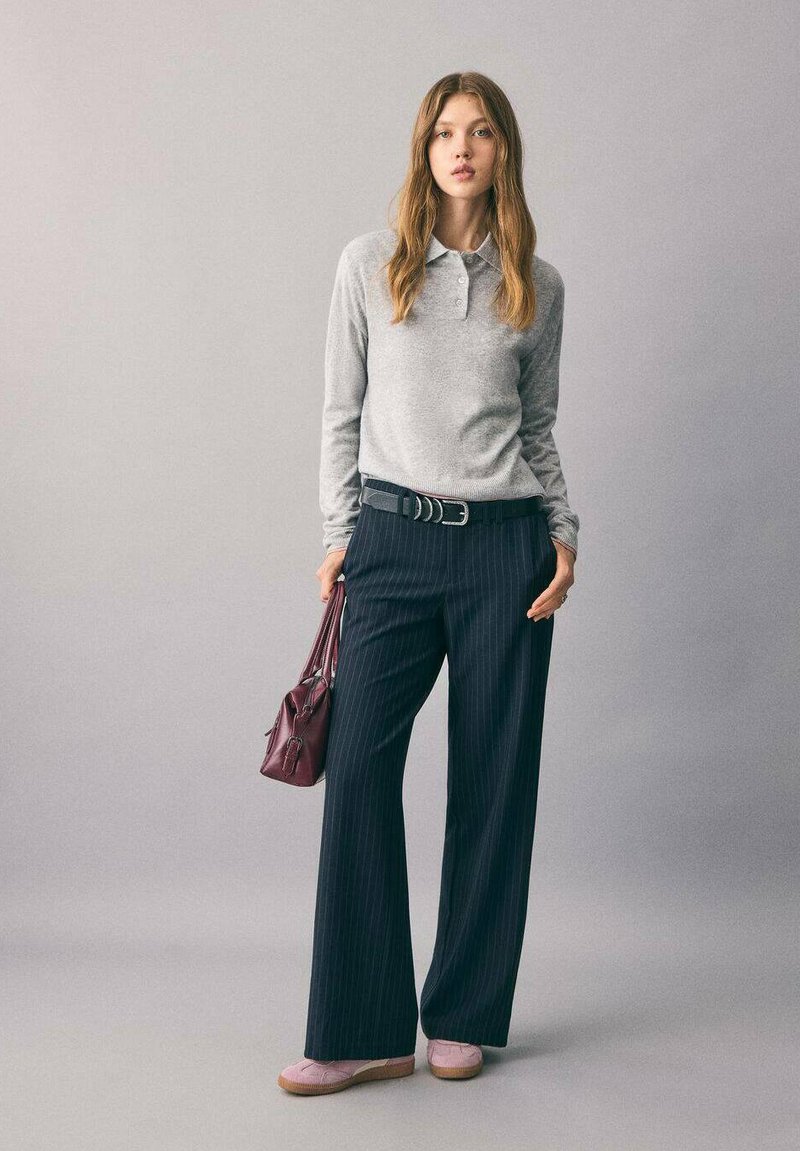 Polo grigio a maniche lunghe, pantaloni a gamba larga a righe, scarpe rosa slip-on e borsa bordeaux. Materiali eleganti e tattili.