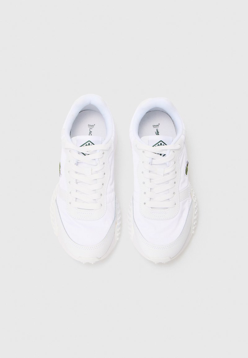 Para białych sneakersów na sznurówki z teksturowanymi podeszwami i zielonym logo z boku, widziana z góry na jasnoszarym tle.