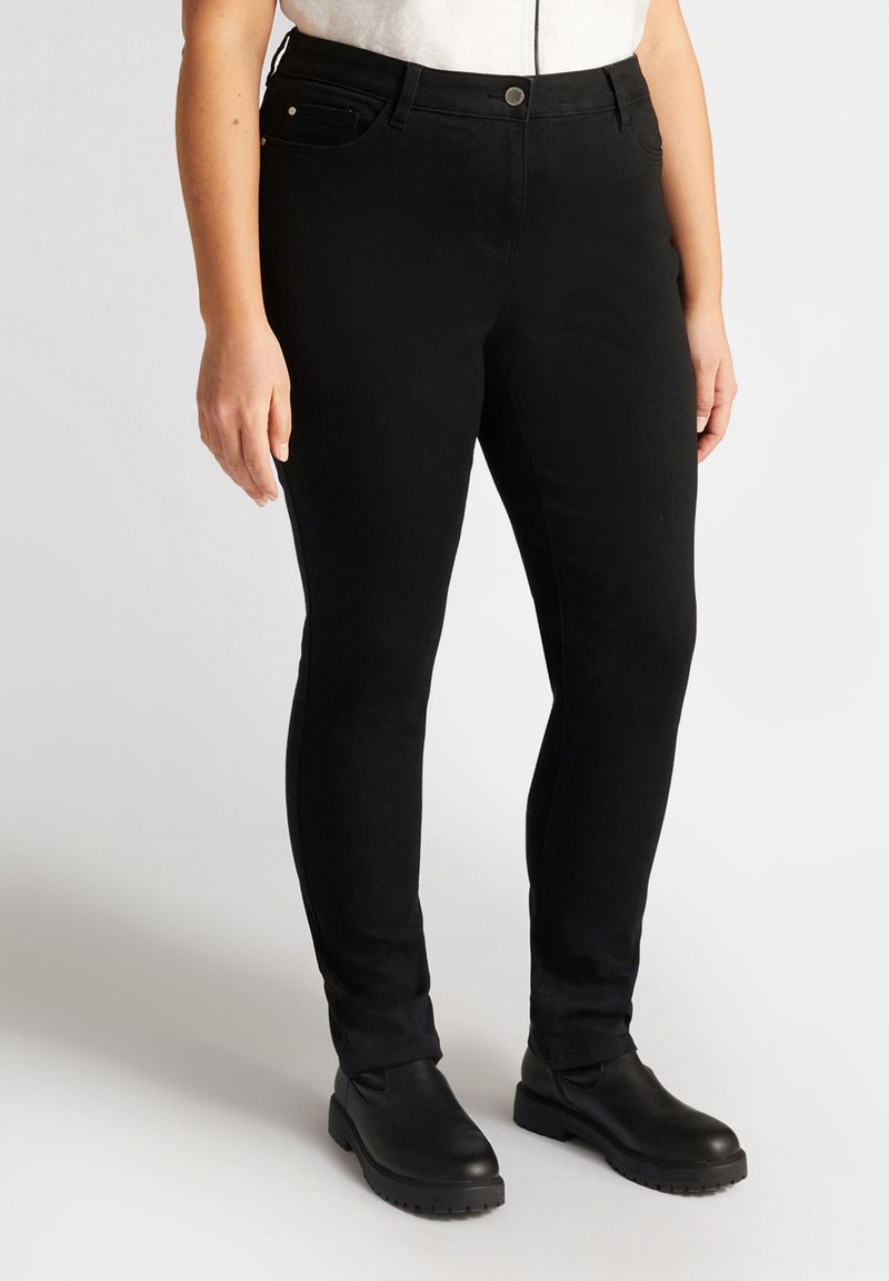Jean skinny noir en denim extensible, avec une taille haute, des poches avant et une texture lisse, associé à des bottines noires.
