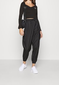 Top corto nero a maniche lunghe con scollatura a V e logo ricamato, abbinato a pantaloni cargo neri larghi e sneakers bianche.