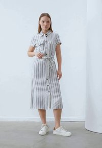 Vestito a righe con bottoni in tessuto leggero, caratterizzato da maniche corte, due tasche sul petto, vita con cintura e orlo al ginocchio.