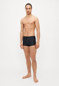 Shorts de bain noirs avec une taille à cordon, design ajusté, coutures minimales, texture lisse et longueur mi-cuisse.