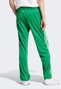 Green athletic pants made of smooth fabric, featuring white side stripes and an elastic waistband. The cut is loose and relaxed.