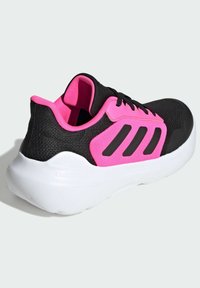 Chaussure de sport noire avec une tige texturée, des accents roses et des rayures noires, dotée d'une semelle blanche rembourrée.