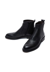 Stivaletti neri in pelle con finitura liscia, chiusura con zip laterale e tacco leggero. Punta arrotondata e motivo testurizzato sulla tomaia.