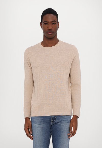 Beige knitted sweater with ribbed texture, crew neckline, and long sleeves, paired with blue denim jeans.