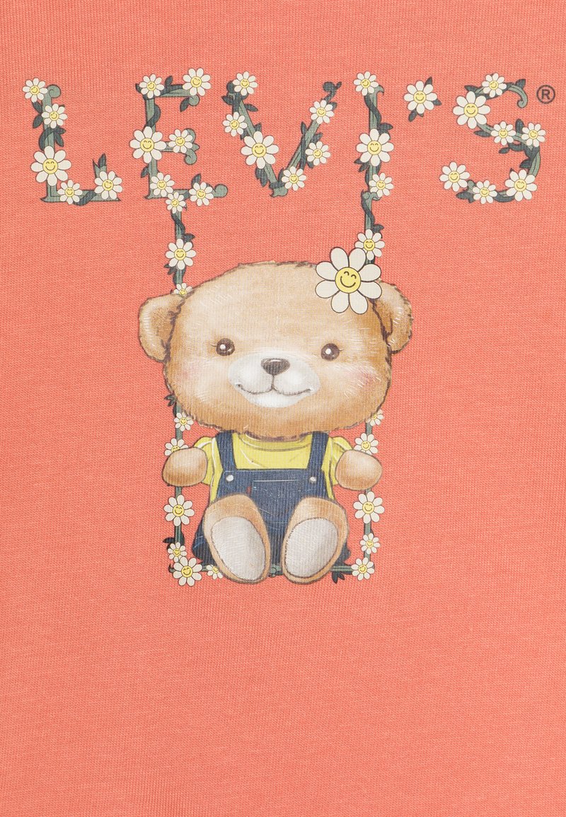 T-shirt corallo con un orso cartoon in salopette di jeans e una maglietta gialla, circondato da decorazioni floreali con il testo "LEVI'S".