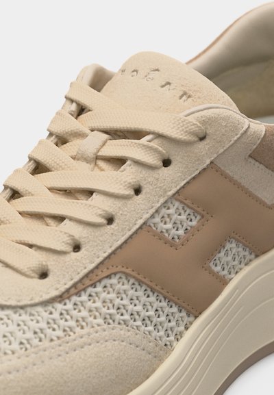 Baskets beiges avec mesh tissé, détails en suède, semelle épaisse, logo "H" en cuir marron sur le côté et lacets plats beiges noués sur le devant.