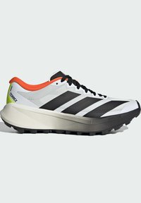 Chaussure de sport blanche avec des rayures noires, des accents orange, une semelle texturée et un design léger. Présente une silhouette élégante et un talon prononcé.