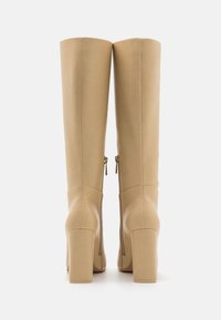 Beżowe kozaki do kolan, wykonane z gładkiego materiału syntetycznego, z grubej pięcie i bocznymi zamkami błyskawicznymi ułatwiającymi zakładanie.
