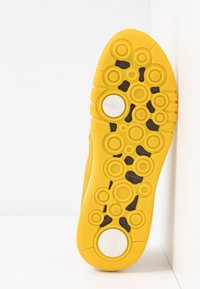 Semelle de chaussure jaune avec des motifs de bande de roulement circulaires, des inserts texturés noirs et des accents circulaires blancs, conçue pour l'adhérence et le confort.