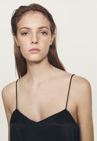 Camisola in satin nera con spalline sottili, caratterizzata da un design a scollo a V e una superficie liscia. Pelle visibile sulle spalle e sull'area della clavicola.