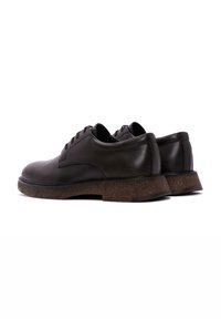 Chaussures noires en cuir avec une finition lisse, à bout arrondi et quatre œillets pour les lacets. Présentent une semelle extérieure marron texturée et des coutures discrètes.