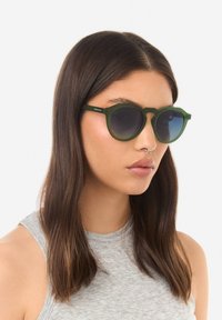 Žalios spalvos apvalūs akiniai nuo saulės su matinio paviršiaus ir gradientinėmis lęšiais. Plonos kojelės su subtiliu prekinio ženklo detalum.