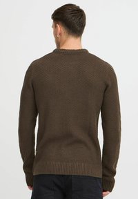 Brauner Strickpullover mit strukturiertem Muster, geripptem Kragen und Bündchen, entworfen für eine figurbetonte Passform. Sichtbare Nähte an den Schultern.