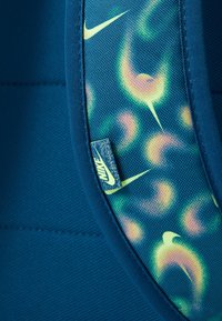 Tejido azul con un acabado texturizado que presenta un patrón abstracto multicolor. Se adjunta una pequeña etiqueta de Nike con un logotipo.