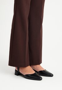 Décolleté slingback in pelle nera con tacco leggero e punta appuntita, abbinate a pantaloni larghi marroni. Texture liscia, design minimalista.