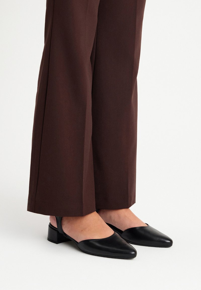 Mustad nahast slingback-kontsad väikese kanna ja terava varbaga, kombineerituna pruuni laiade säärtega pükstega. Sile tekstuur, minimalistlik disain.