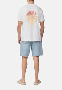 Witte katoenen t-shirt met een roze en oranje ronde afbeelding op de achterkant, met tekst en coördinaten. Draag het met lichtblauwe denim shorts.