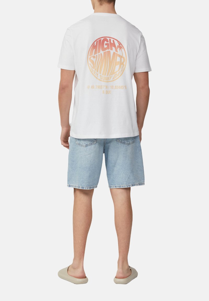 Witte katoenen t-shirt met een roze en oranje ronde afbeelding op de achterkant, met tekst en coördinaten. Draag het met lichtblauwe denim shorts.
