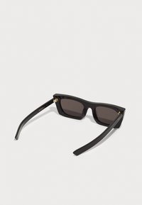 Black sunglasses with a rectangular frame, dark lenses, and gold accents on the hinges. The design features smooth, glossy texture.