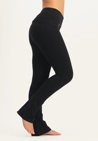 Svarta utsvängda leggings med en bred, hög midjeresår, tillverkade av elastiskt material. Designen har en åtsittande siluett som sträcker sig ned till anklarna.